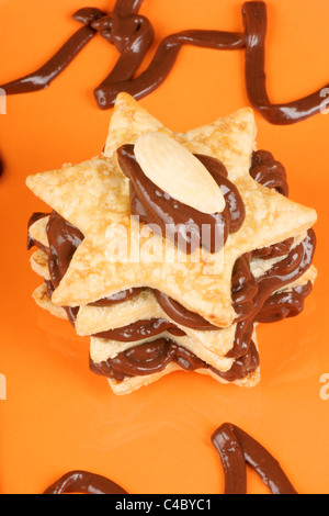 Sternförmige Schokolade Sahne und Mandeln Millefeuille über eine orange Platte. Selektiven Fokus. Stockfoto