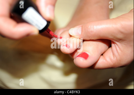Frau malt ihre Zehen Nägel Rot Stockfoto