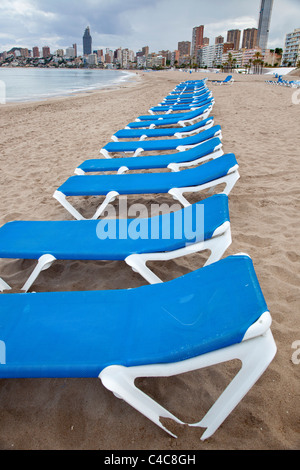 Eine Reihe von leeren blauen und weißen liegen am Strand in Benidorm, Spanien vor dem Hintergrund der Hochhaus-Hotels. Stockfoto