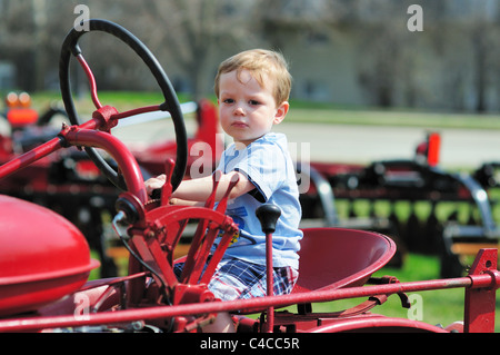 Schwere kleine Junge lächelt als er genießt eine imaginäre Fahrt auf einem Traktor auf einem lokalen Farm Bureau einen Traktor Ereignis berühren. Illinois, USA. Stockfoto