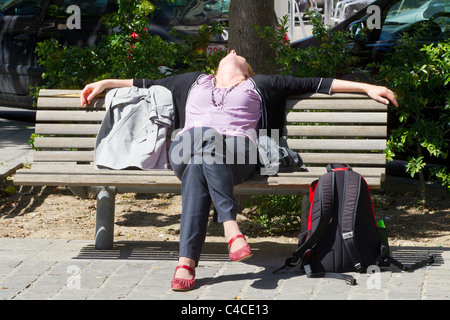 Junge Frau, die allein auf der Parkbank sitzt und sich entspannt Stockfoto
