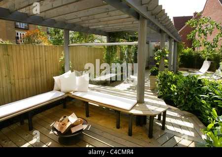 zeitgenössische moderne englische Stadtgarten mit Holzbank decking und Pergola, Wind Pause Glas und Feuerkorb tagsüber Stockfoto