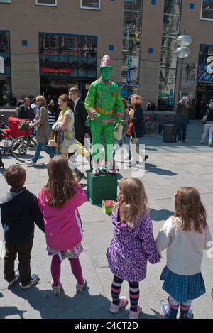 A Street Performer in einem alle grünen Outfit gekleidet führt für Kinder im Grundschulalter im Alter in der waqs in München, Deutschland Stockfoto