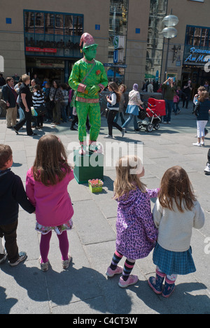 A Street Performer in einem alle grünen Outfit gekleidet führt für Kinder im Grundschulalter im Alter in der waqs in München, Deutschland Stockfoto