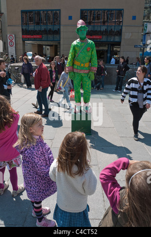 A Street Performer in einem alle grünen Outfit gekleidet führt für Kinder im Grundschulalter im Alter in der waqs in München, Deutschland Stockfoto