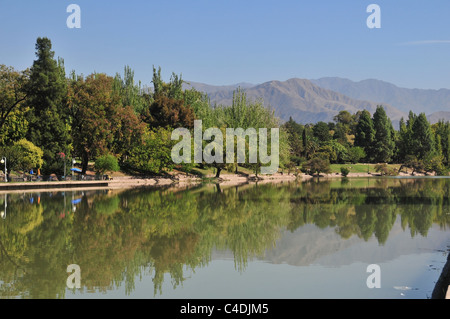 Blauer Himmelsblick in Richtung Anden, von grünen Bäumen Reflectiing im Wasser Lago del Parque, Park General San Martin, Mendoza, Argentinien Stockfoto