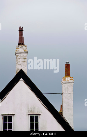 Ein weißes Haus mit zwei hohen Schornsteine und Schornstein. Ein Schornstein ist gegen das Hausdach verspannt. Stockfoto