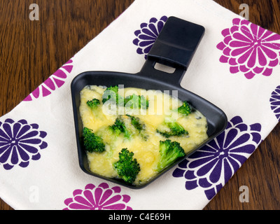 Raclettepfännchen mit Käse und Broccoli auf bunte Serviette Stockfoto