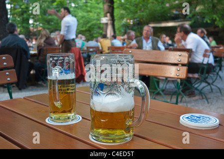 Eine typische sehr große Bierkrug neben ein viel kleineres Bierglas auf einem Tisch im Biergarten Augustiner-Keller in München. Stockfoto