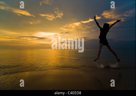 Ein Junge springt vor Freude und genießen ihre Freiheit am Strand bei Sonnenuntergang. Aufgenommen am Phra Ae Beach, Koh Lanta, Thailand