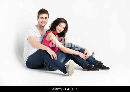 glückliches Paar sitzen neben Wand lächelnd Stockfoto