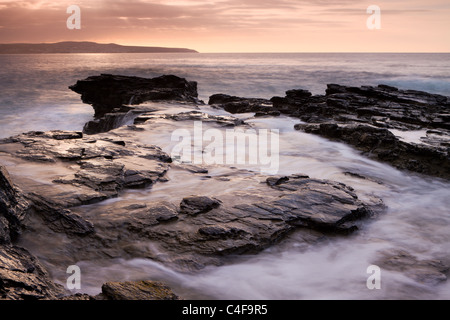 Wellen über die Felsen von Godrevy Point bei Sonnenuntergang, Cornwall, England. Herbst (Oktober) 2009. Stockfoto