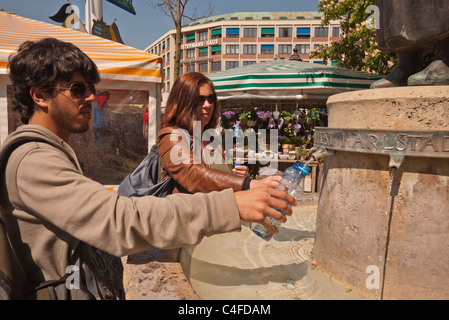 Ein Mann und eine Frau füllen ihre Wasserflaschen aus dem öffentlichen gut gelegen am Viktualienmarkt Münchens im freien Markt. Stockfoto