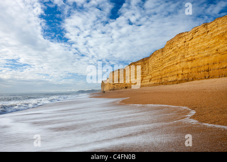 Wellen Waschen sauberer Bienenstock Strand unterstützt von hoch aufragenden Sandsteinfelsen, Burton Bradstock, Dorset, England. Winter (Februar) 2011. Stockfoto