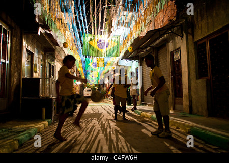 Kinder spielen Fußball in Favela da Mare in Rio De Janeiro, Brasilien. Straßendekoration für die WM 2010. Brasilien-Flagge Stockfoto