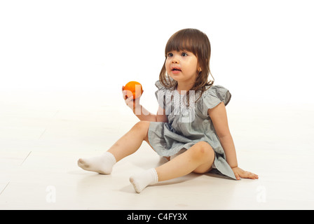 Begeistert kleine Mädchen am Boden hält Mandarin Obst und wegsehen Stockfoto