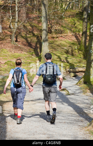 Paar tragen Rucksäcke zusammen gehen auf einem Wald Wanderweg halten sich an den Händen in Wäldern in Lake District National Park, Cumbira, England, UK. Stockfoto