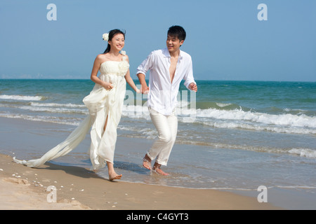 Glückliche Brautpaar laufen am Strand Stockfoto