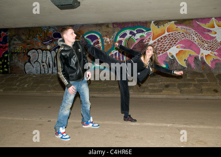 Die Szene zeigt, wie sich eine junge kaukasische Frau in der Unterführung in Bristol mit Tae kwon in der Kampfkunst gegen einen Angreifer verteidigt Stockfoto