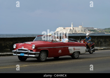 Ford Mercury Taxi fährt entlang des Malecon in Havanna, Kuba mit einem Leuchtturm im Hintergrund. © Craig M. Eisenberg Stockfoto