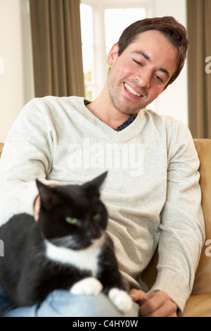 Glücklicher junger Mann mit Katze auf sofa Stockfoto