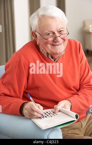 Senior woman Entspannung im Stuhl zu Hause ausfüllen Kreuzworträtsel Stockfoto