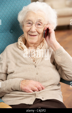 Ältere Frau am Handy zu Hause im Sessel sitzen Stockfoto