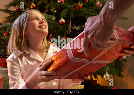 Junge Mädchen erhalten Weihnachtsgeschenk vor Baum Stockfoto