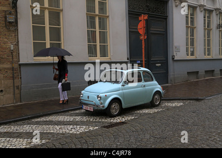 Frau mit Regenschirm übergibt einen alten Fiat 500 parkten in einer Seitenstraße in Brügge, Belgien. Stockfoto