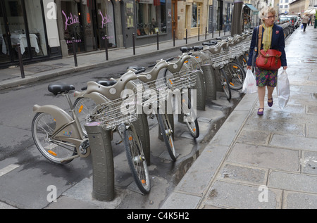 Eine Frau geht durch eine Reihe von Velib Zyklen (eine öffentliche Fahrrad Vermietungsprogramm) in einer Paris Straße. Stockfoto