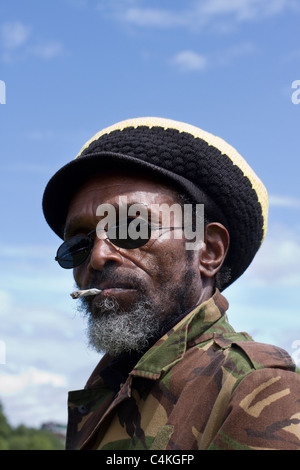 Tam (MR) Rauchen & tragen Rasta Kammgarn Motorhaube, Rasta und Reggae headwear einschließlich Hüte, Mützen, Caps, strotzt, Tams, fedoras, Schals und dreadlock Perücke Hüte in Afrika Oye Event in Sefton Park Liverpool UK größte freie Afrikanische Musik Festival Stockfoto