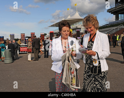 Weibliche Racegoers bei einem Goodwood Abend treffen im Juni Lesen der Racing Post versucht, einen Gewinner UK Stockfoto