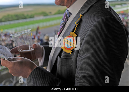 Racegoers bei einem Goodwood Abend treffen im Juni Lesen der Racing Post versucht, einen Gewinner UK Stockfoto