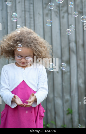 Ein kleines Mädchen spielt in ihrem Garten, um Luftblasen zu fangen versuchen. Stockfoto