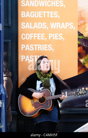 Junge Sängerin als Straßenmusikant mit einer Gitarre, Aberystwyth, Wales. Stockfoto