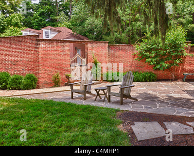 Cape Cod Stil Holzstühle auf Crazy Pflasterung Terrasse vor Ziegel Wand und Garten Tor Stockfoto