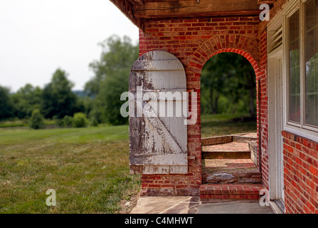 Alte weiße lackierte Tür in hellen roten Backsteinmauer öffnet sich Garten und Bäumen Stockfoto