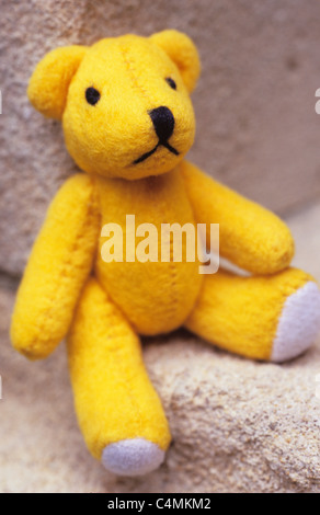 Nahaufnahme eines gelben Teddybär sitzend auf und lehnte sich zurück gegen strukturierte Steinflächen Stockfoto