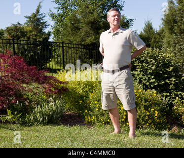 Baby-Boomer sitzen auf dem Rasen und auf der Suche nach Unkraut in ein Blumenbeet Stockfoto