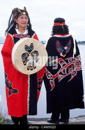 Zwei Tlingit Indianer Frauen zeigen traditionelle Umhänge mit Knöpfen und eine Trommel des Keex-Stammes (Kwaan) an Kake, Alaska, USA entwickelt. Stockfoto