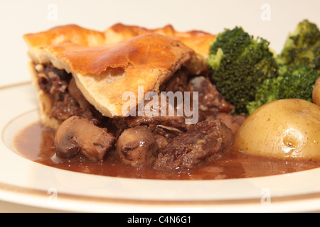 Hausgemachte Steak und Mushroom pie mit einem goldenen Blätterteig Kruste mit gekochten Kartoffeln und Brokkoli portioniert und auf einem Teller serviert. Stockfoto