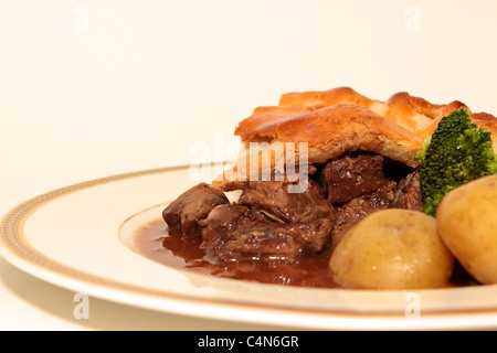 Hausgemachte Steak und Mushroom pie mit einem goldenen Blätterteig Kruste mit gekochten Kartoffeln und Brokkoli portioniert und auf einem Teller serviert. Stockfoto