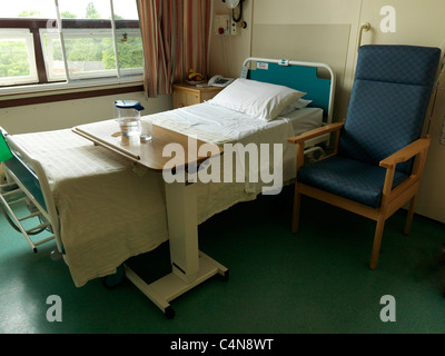 Elektrisch verstellbare Krankenhausbett mit Tisch und Stuhl von der Seite Stockfoto