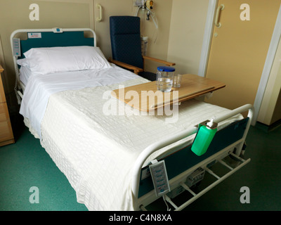 Elektrisch verstellbare Krankenhausbett mit Tisch und Stuhl von der Seite Stockfoto