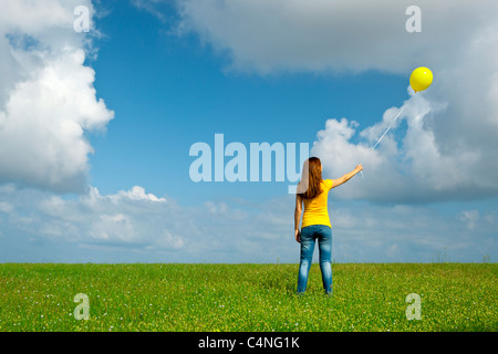 Glückliche junge Frau mit einem gelben Ballon auf der grünen Wiese Stockfoto