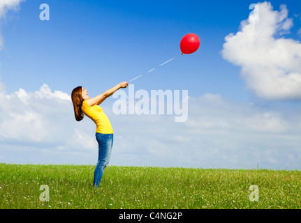 Glückliche junge Frau mit einem roten Ballon auf der grünen Wiese Stockfoto