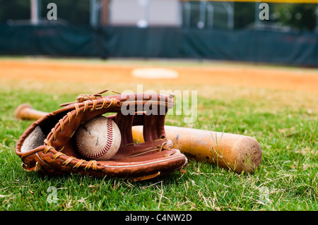 Baseball, Handschuh und Fledermaus auf Feld mit Sockel und Feldspieler im Hintergrund. Stockfoto