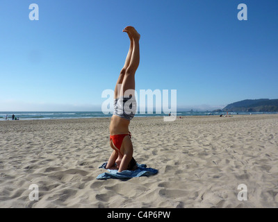 Junge Frau in Yoga Kopfstand auf sonnigen Tag in Cannon Beach, Oregon, USA Stockfoto