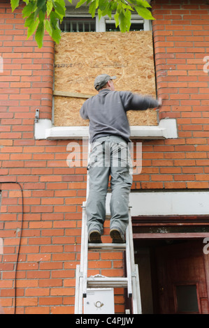 Ein Mann auf einer Leiter besteigen Sie ein Fenster im oberen Stock Stockfoto