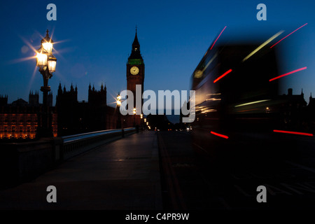 Eine untergehende Sonne Silhouetten der Houses of Parliament und Big Ben in London, England. Ein roter Bus fährt helle Streifen, wie es geht. Stockfoto